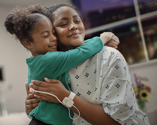 Patient in hospital gown hugging small child.