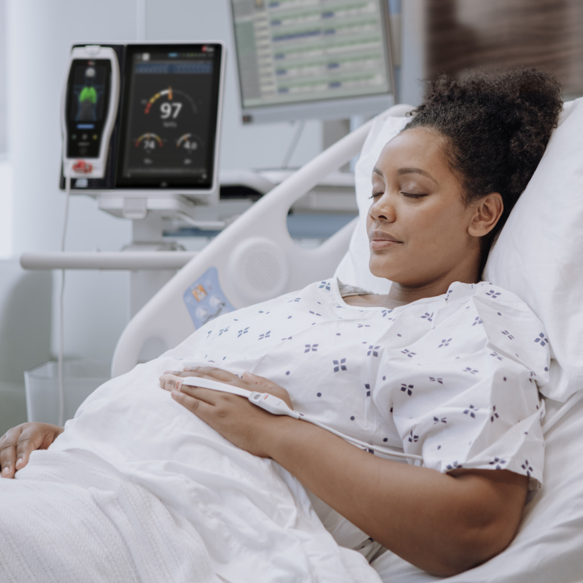 Dark-skinned patient in hospital bed being monitored with a Masimo RD SET pulse oximetry sensor and Radical-7 pulse oximeter docked in a Root device.