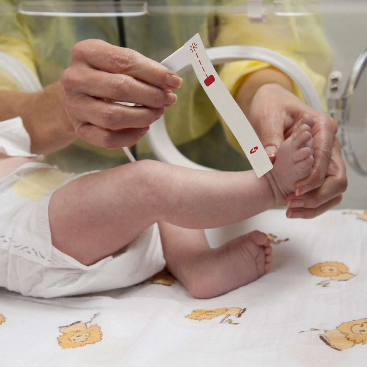 Infant in incubator in a hospital neonatal intensive care unit with a clinician applying a Masimo pulse oximetry sensor. 