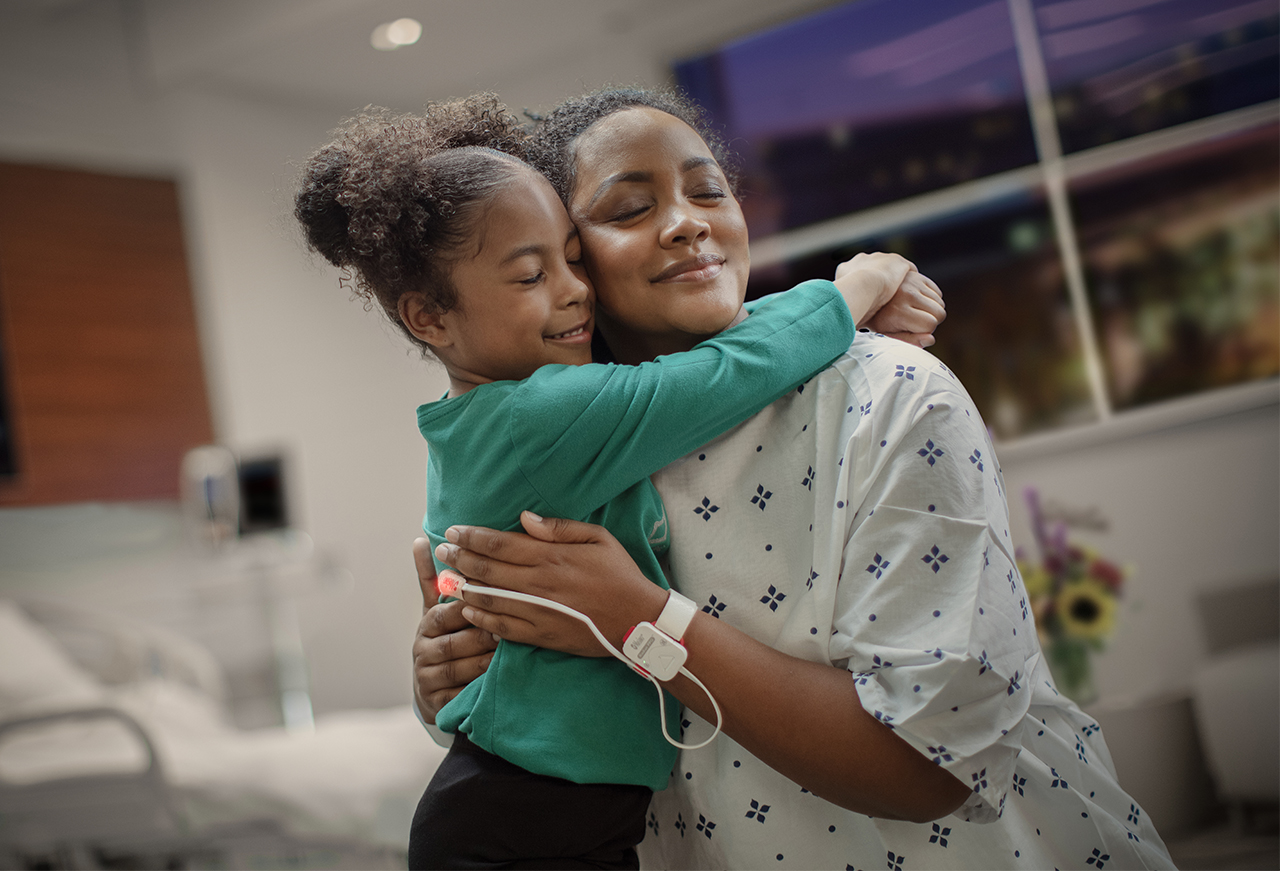 Mother embracing her child in a hospital setting while a Masimo sensor tracks her oxygen levels.